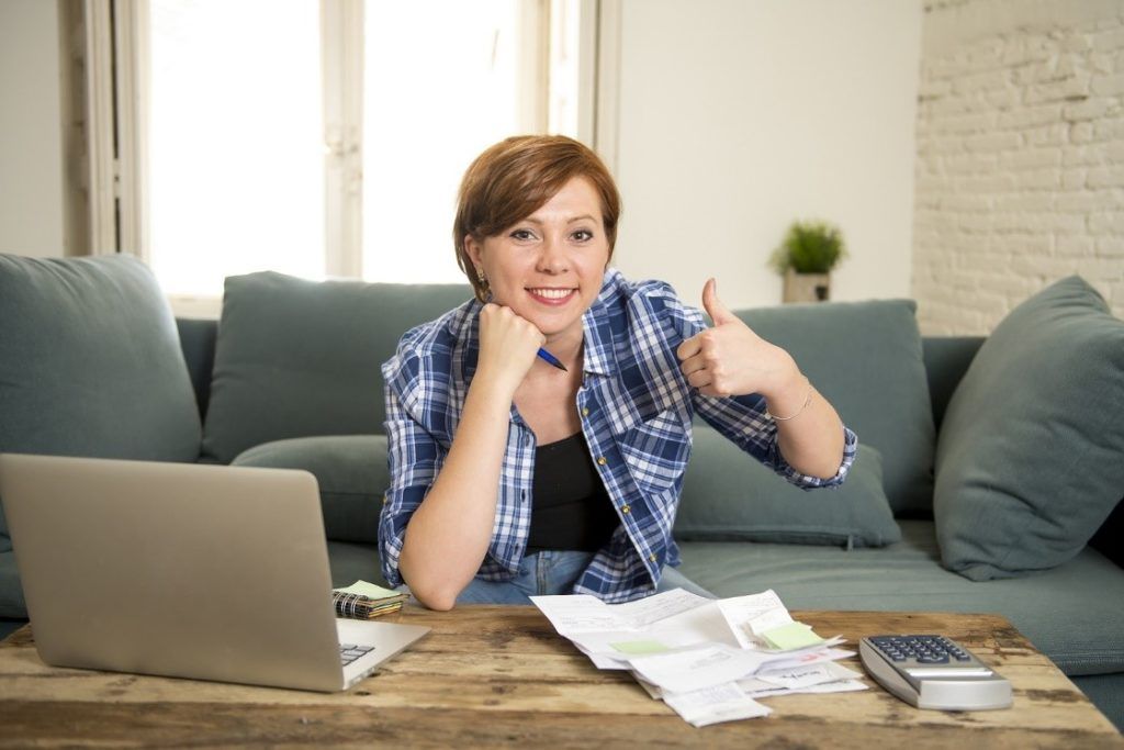 woman banking and accounting home monthly and credit card expenses with computer laptop doing paperwork smiling relaxed in financial success