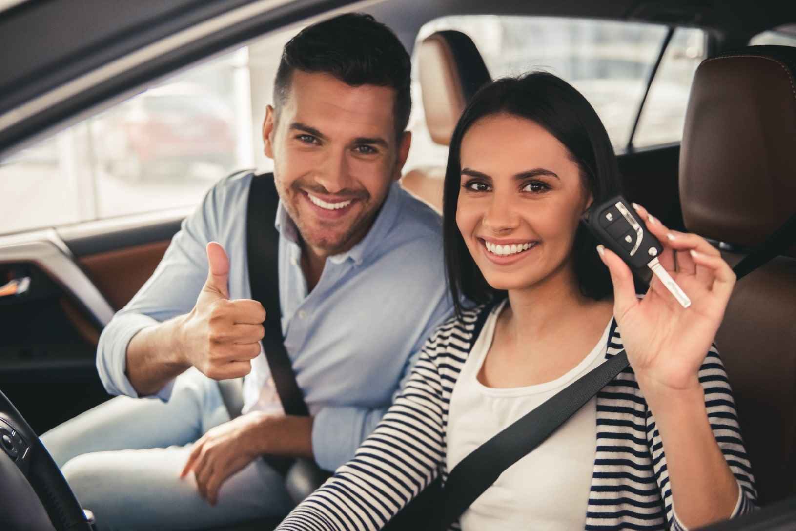 Couple holding a car key looking at camera and smiling while sitting in their new car