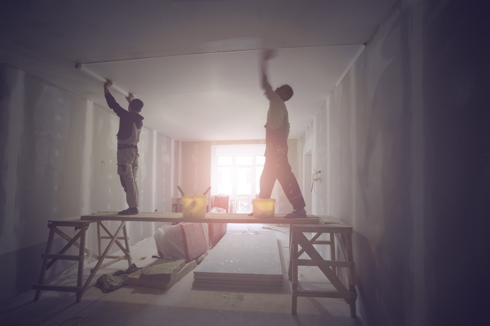 Two construction workers install a ceiling in a home renovation