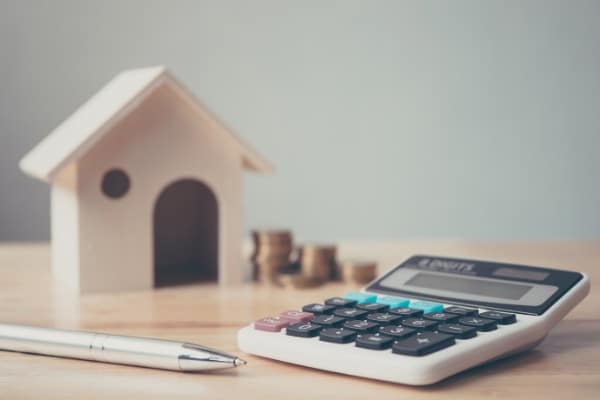 Calculator with wooden house and coins stack and pen on wood table