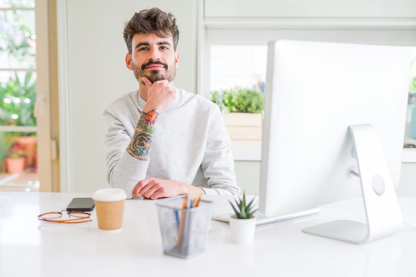 Young man working using computer with hand on chin thinking about taking out a personal loan