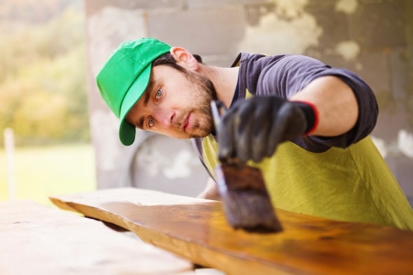 Man varnishing wooden planks and doing home renovation outside the house