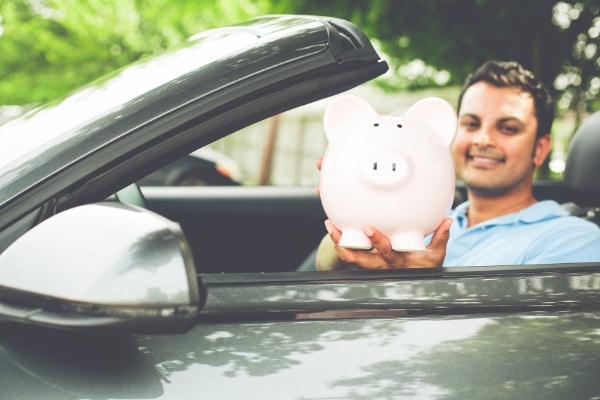 Man sitting in a car holding a piggy bank