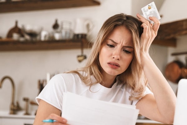 Stressed women holding a plastic credit card while looking at paper documents