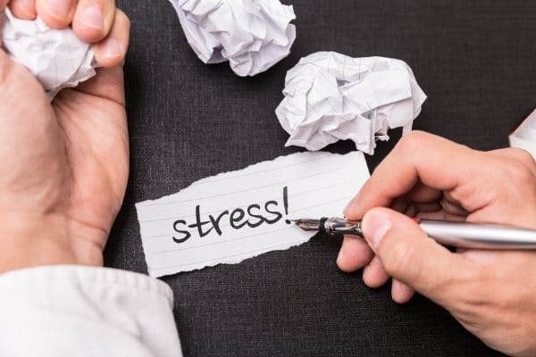 Crumpled paper balls and Man’s hand with black writing word “stress”