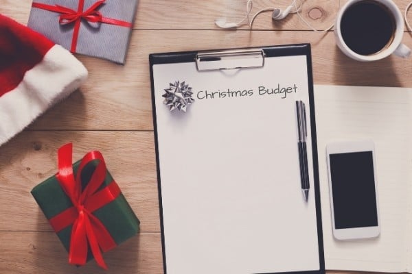 Pen, wrapped gifts, Santa hat, phone and notebook with words “Christmas budget”