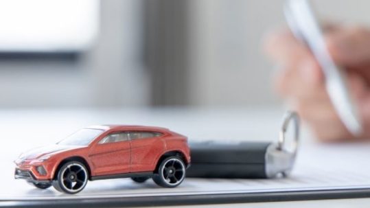 A person’s hand signing car loan agreement contract with toy car on desk