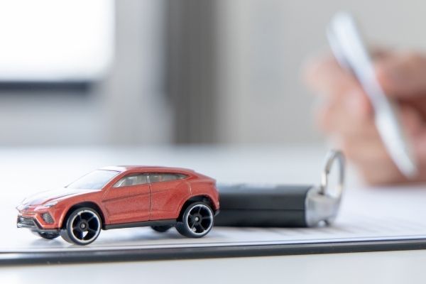 A person’s hand signing car loan agreement contract with toy car on desk