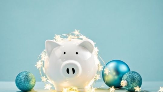 White piggy bank wrapped in a string of Christmas lights over a blue background
