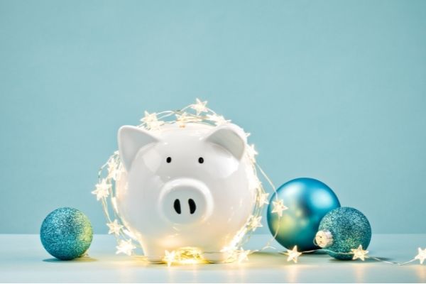 White piggy bank wrapped in a string of Christmas lights over a blue background