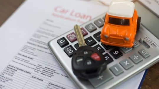 A car model, a car key and a calculator placed on top of car loan application.