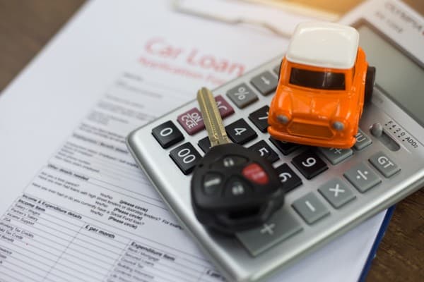 A car model, a car key and a calculator placed on top of car loan application.